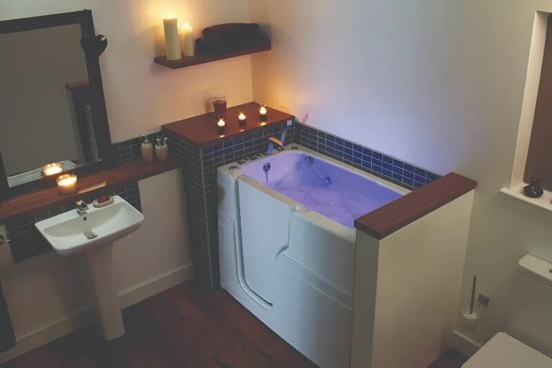 White walk-in bath with purple chromotherapy lighting surrounded by candles in a dimly lit bathroom