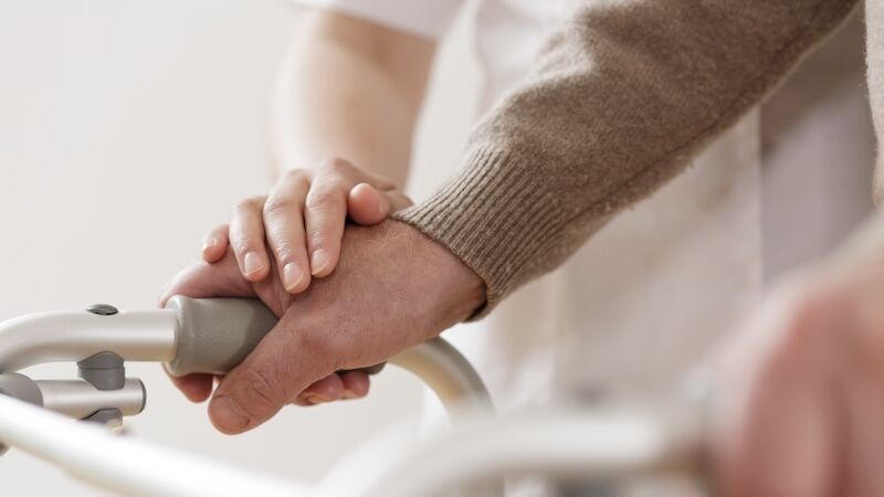 A caregiver gently places their hand on an elderly persons hand, which is gripping a walker, offering support and reassurance.