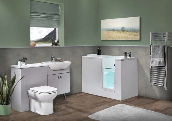 Modern accessible bathroom with a walk-in bathtub, toilet, sink, potted plant, towel rack with folded towels, wall art, and a window with a view of mountains. The decor is minimalist with soft green walls.