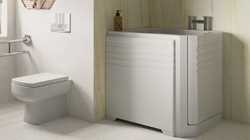 Modern accessible bathroom with a wall-mounted toilet, metal handrail, and a walk-in bathtub with a door and grab bars. There is a bottle of soap on the bathtub ledge. Light-colored walls and floor.