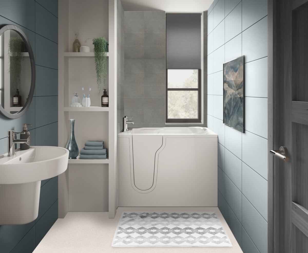 Modern bathroom with blue tile walls, a walk-in bathtub, round mirror above a sink, open shelving with towels and d√©cor, a window with a gray shade, and a patterned rug on the floor.
