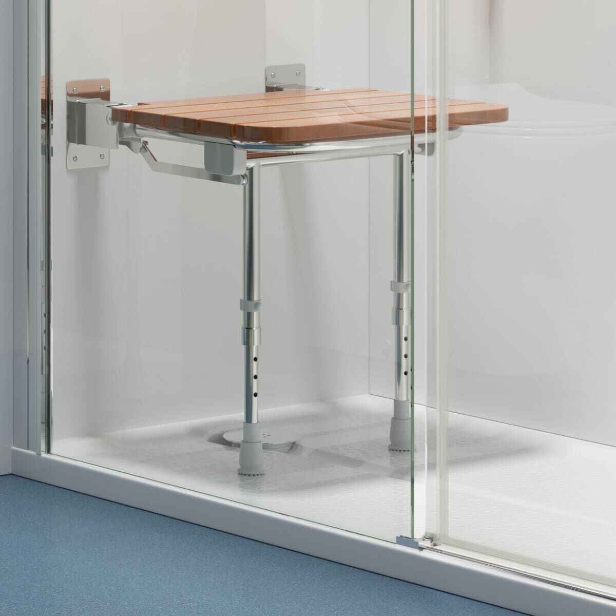 A wooden shower seat with metal legs is mounted on the wall inside a glass shower enclosure. The seat has adjustable legs and is designed for accessibility and support.