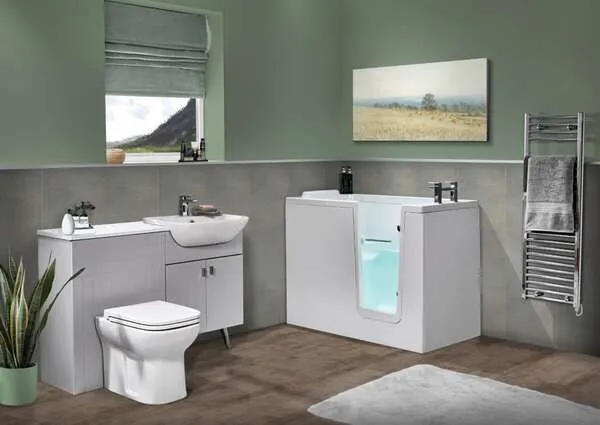 Modern accessible bathroom with a walk-in bathtub, toilet, sink, potted plant, towel rack with folded towels, wall art, and a window with a view of mountains. The decor is minimalist with soft green walls.