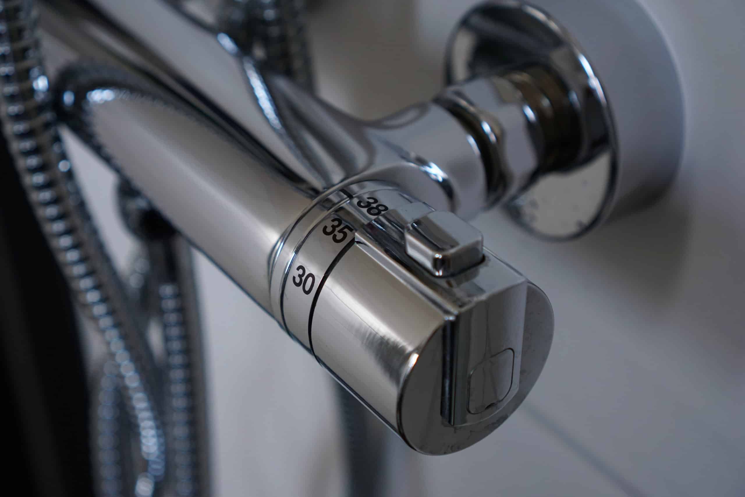 Close-up of a modern metallic shower temperature control knob, showing temperature markings at 30, 35, and 38 degrees Celsius, with reflective chrome finish and flexible hoses visible.