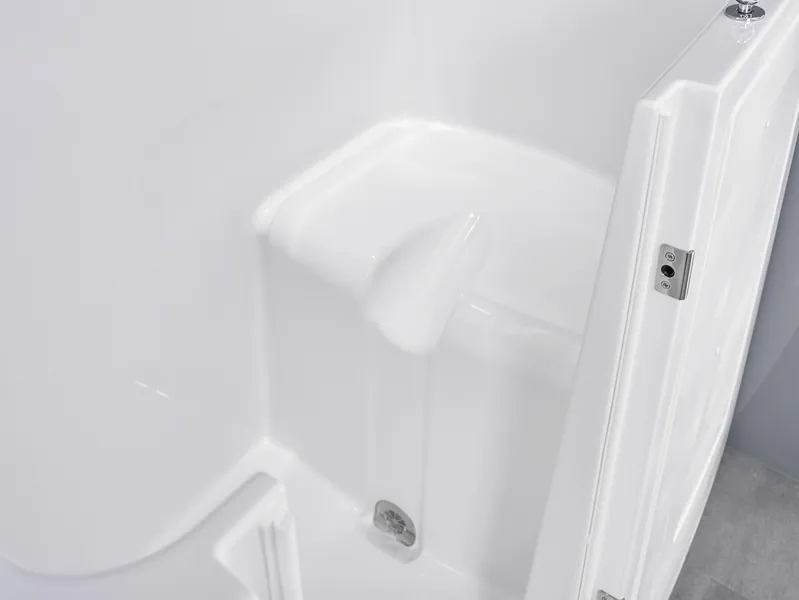 Close-up view of a clean, white walk-in shower with an open door, showing a built-in seat and a drain at the base.