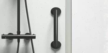 A modern shower with a black showerhead, hose, and control panel on a white speckled wall. A black grab bar is mounted vertically next to the shower fixtures.