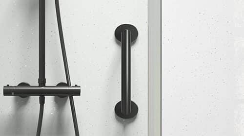 A modern shower with a black showerhead, hose, and control panel on a white speckled wall. A black grab bar is mounted vertically next to the shower fixtures.