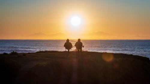 Two people sitting by the sea with a sunset