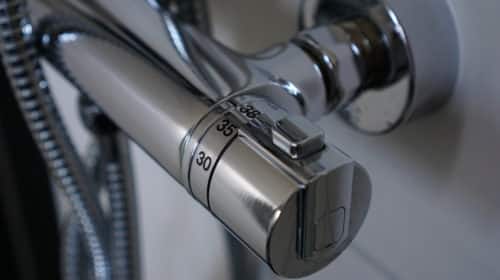 Close-up of a modern metallic shower temperature control knob, showing temperature markings at 30, 35, and 38 degrees Celsius, with reflective chrome finish and flexible hoses visible.