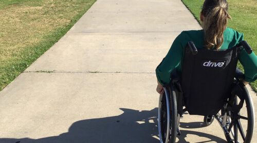 Young woman using a wheelchair in a park footpath