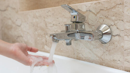A hand taking the temperature of the water coming out of a thermostatic tap