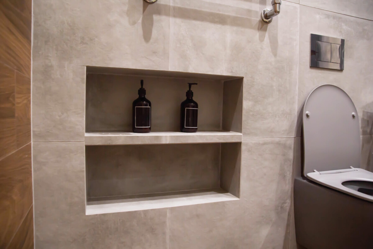 Recesses and shelves for shampoo and shower gel bottles in a gray wall and porcelain tiles in a bathroom.