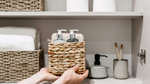 Woman puts wicker box with cosmetics products in bathroom closet