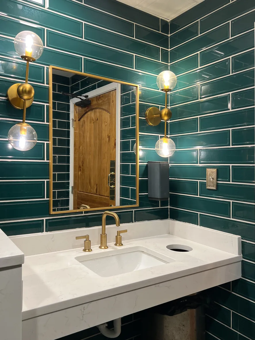 Bathroom with green subway tile walls, featuring a modern sink and minimalist decor.