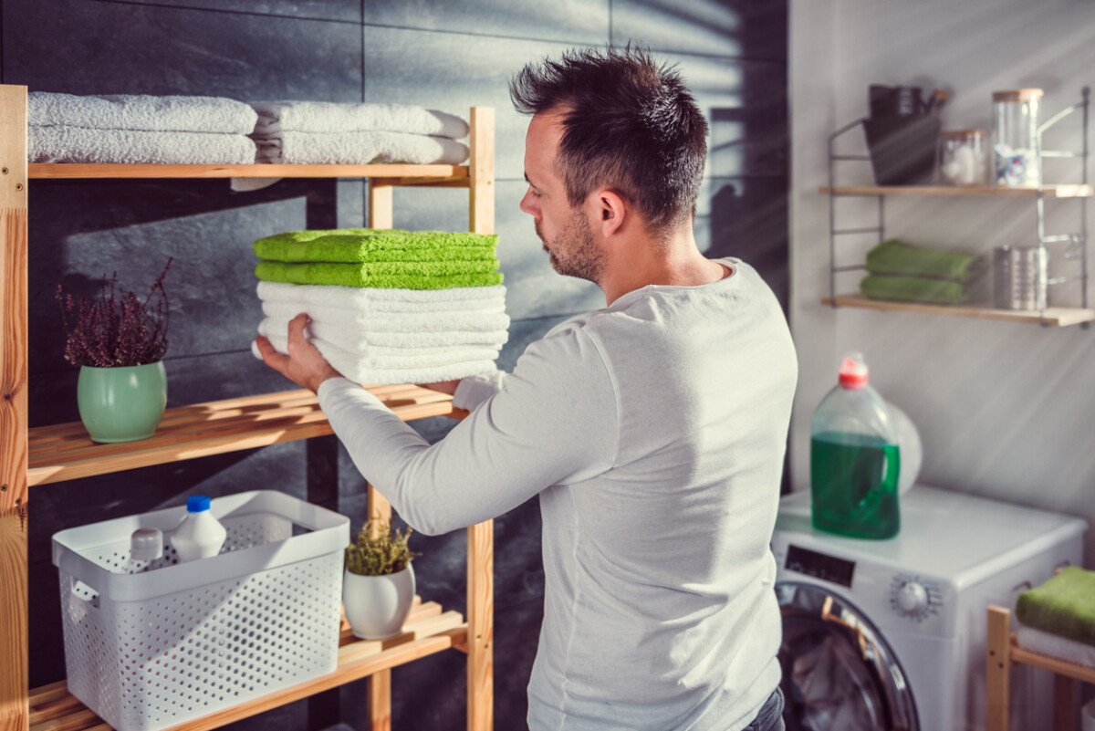 Man arranging clean towels in a laundry room with organised shelves and storage.