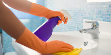 woman doing chores in bathroom at home, cleaning sink and faucet with spray detergent. Cropped view