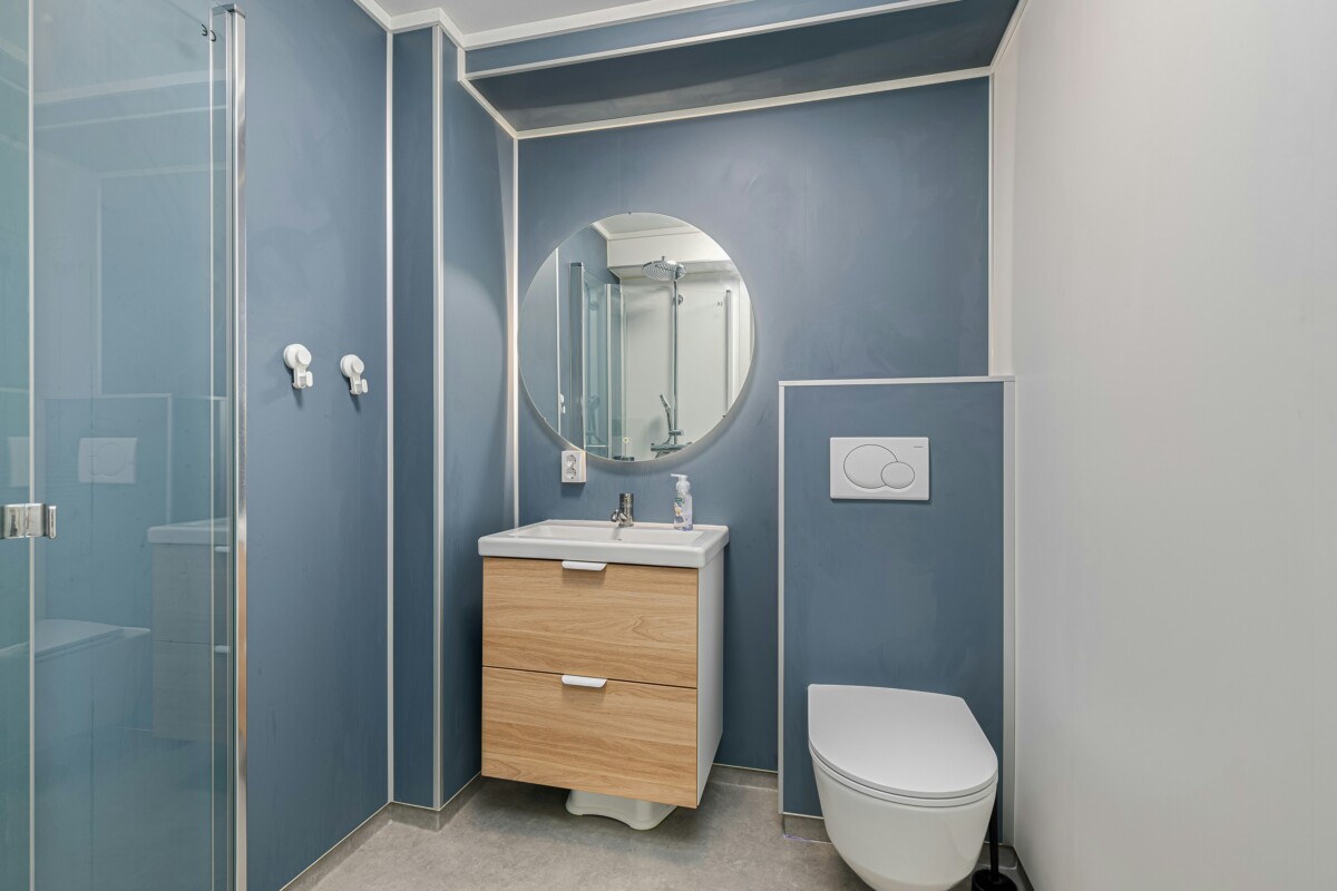A powder blue bathroom with a wooden accent cabinet, white sink and white toilet